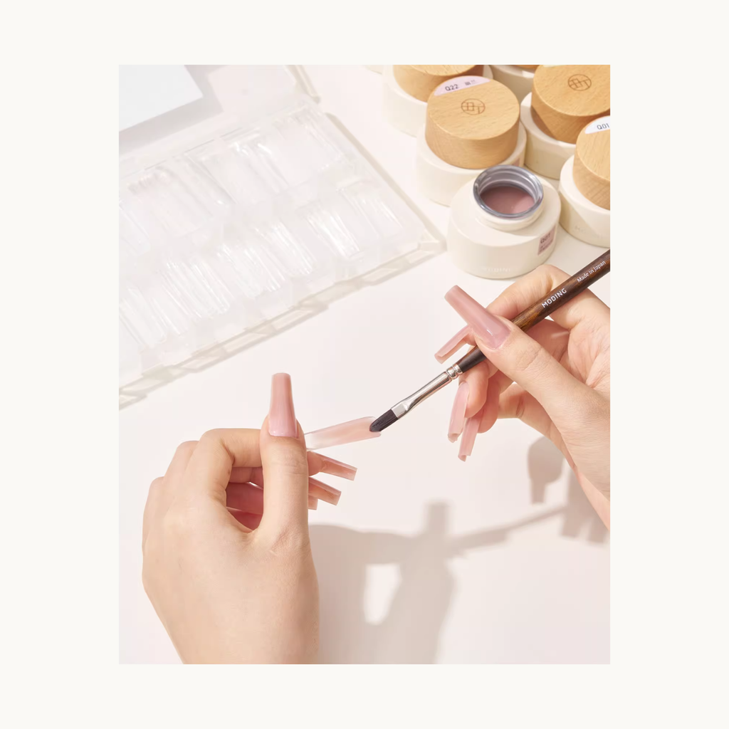 Hand applying MODING colored extension gel onto nail mold tips using a sculpting brush, showing the smooth application process for nail extensions.