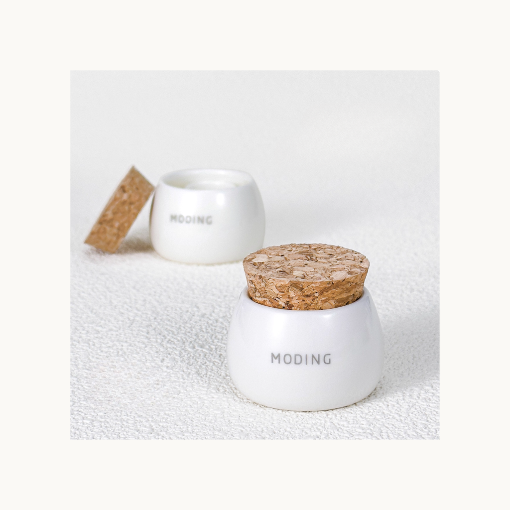 Minimalist display of Moding ceramic brush cleaner cup with cork lid on a clean textured surface.