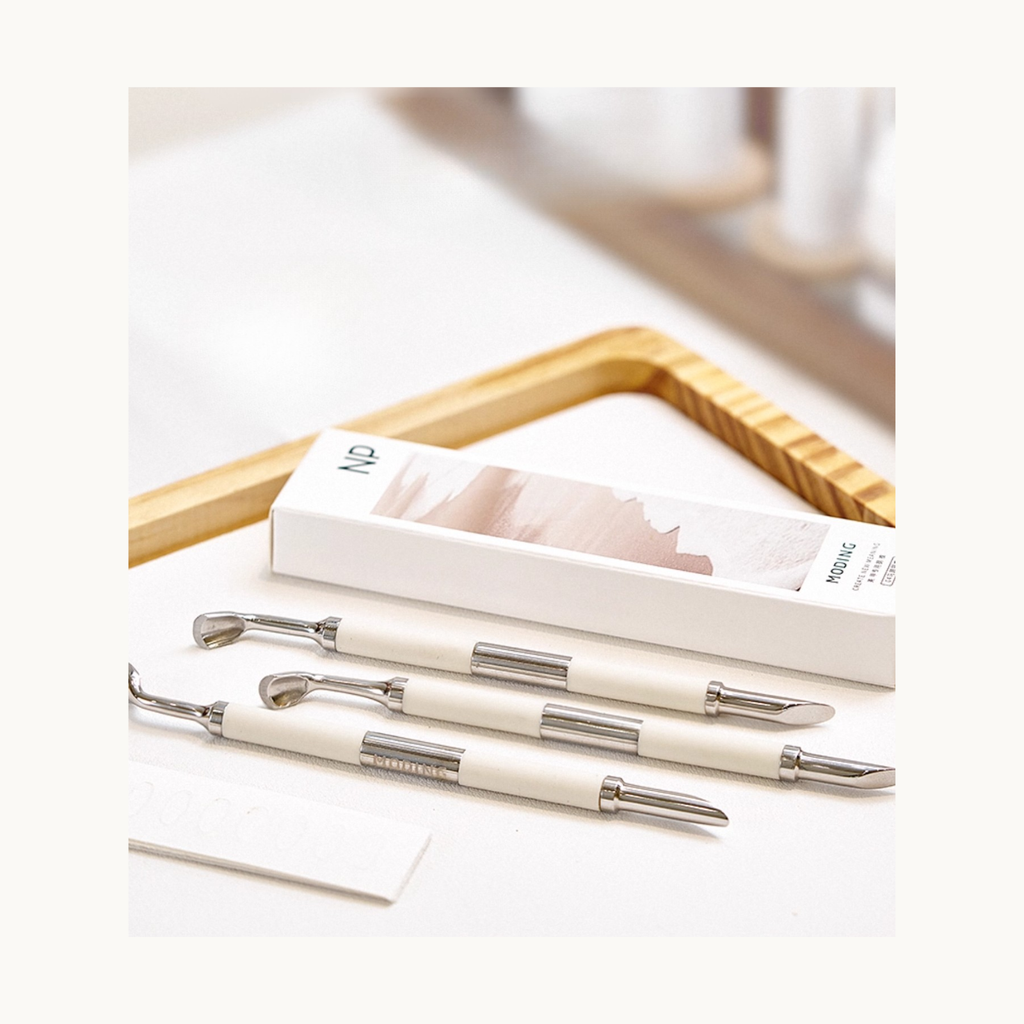 Dual-ended stainless steel nail art tools displayed with the Moding packaging box on a clean minimal workspace.