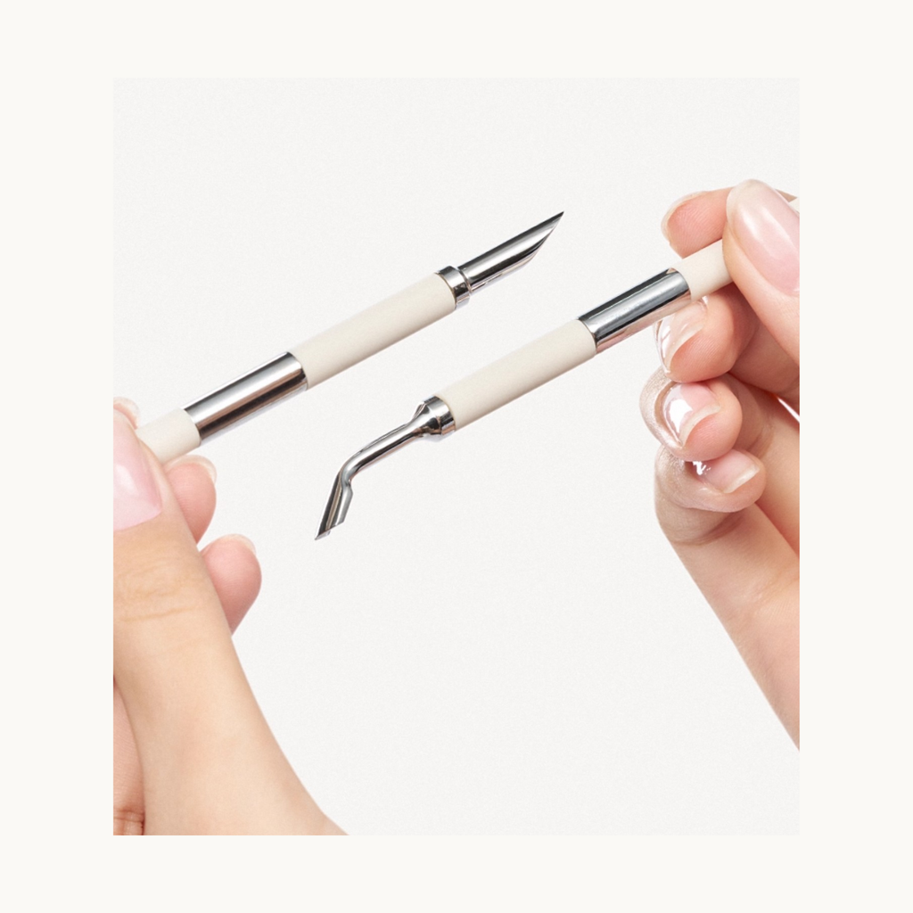 Close-up of hands holding dual-ended stainless steel nail art tools, showing the angled and pointed tips.