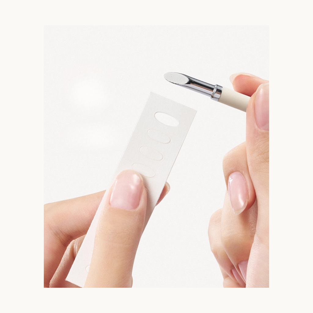 Close-up demonstration of using a dual-ended nail art tool to lift or apply nail adhesive tabs.