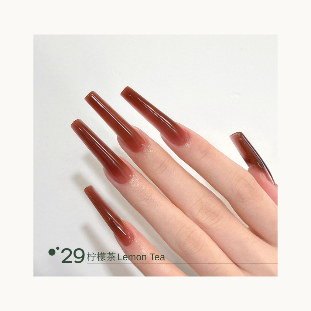Long coffin-shaped nails painted in shade Q29 Lemon Tea, a warm amber-brown tea-toned gradient with a glossy finish.