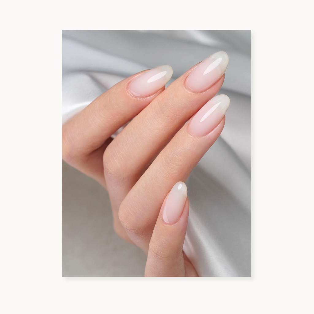 Close-up of a hand with long, almond-shaped nails show the moding Tinted Nude Builder Gel F31 Milky White color with a light background