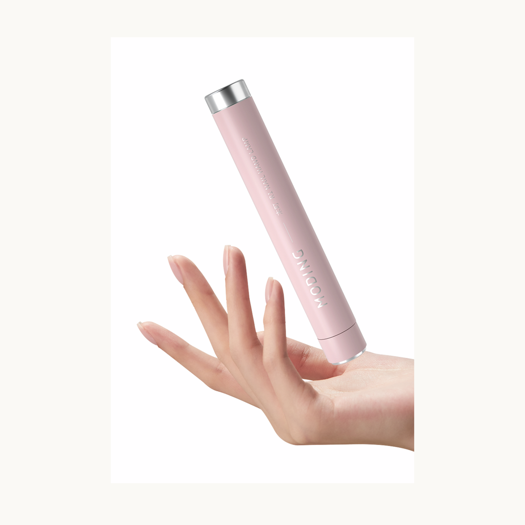 Hand holding a pink MODING portable nail lamp for lightweight usage demonstration