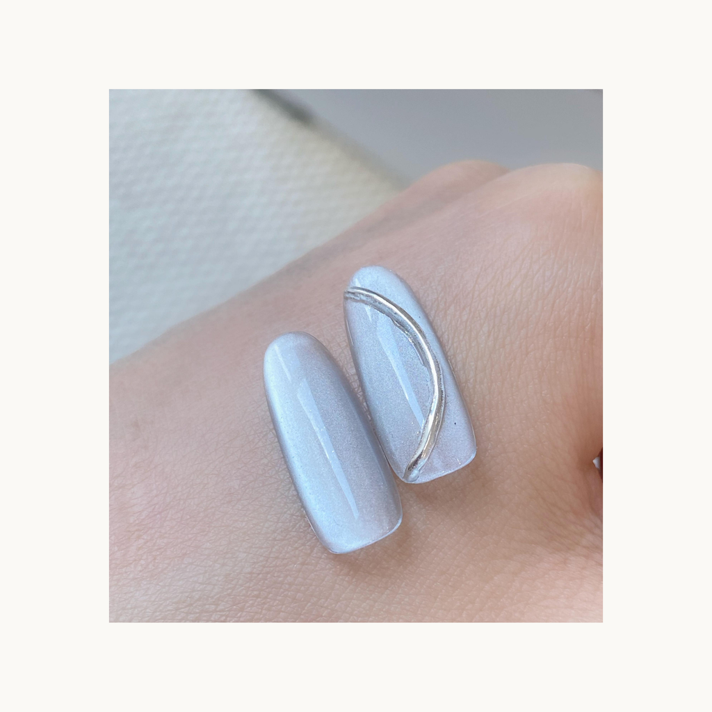 Two nail swatches of Qingyou Waterglow White Cat Eye Gel on hand, featuring soft luminous cat-eye shine.